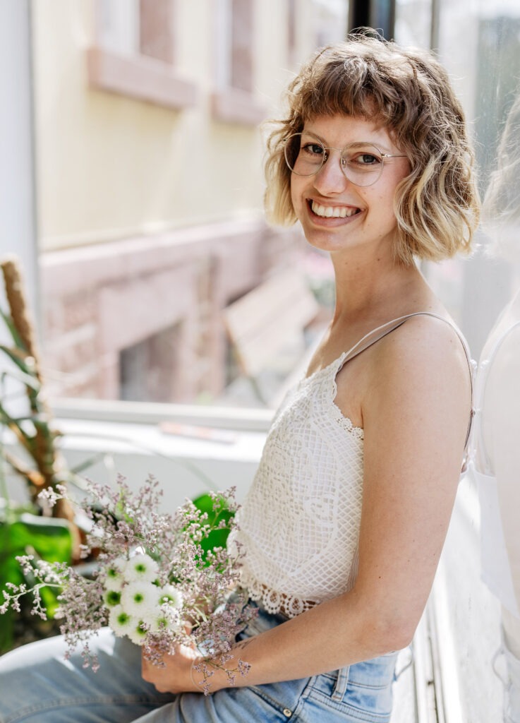 junge Frau sitzt auf einer Fensterbank mit einem Blumenstrauß in der Hand